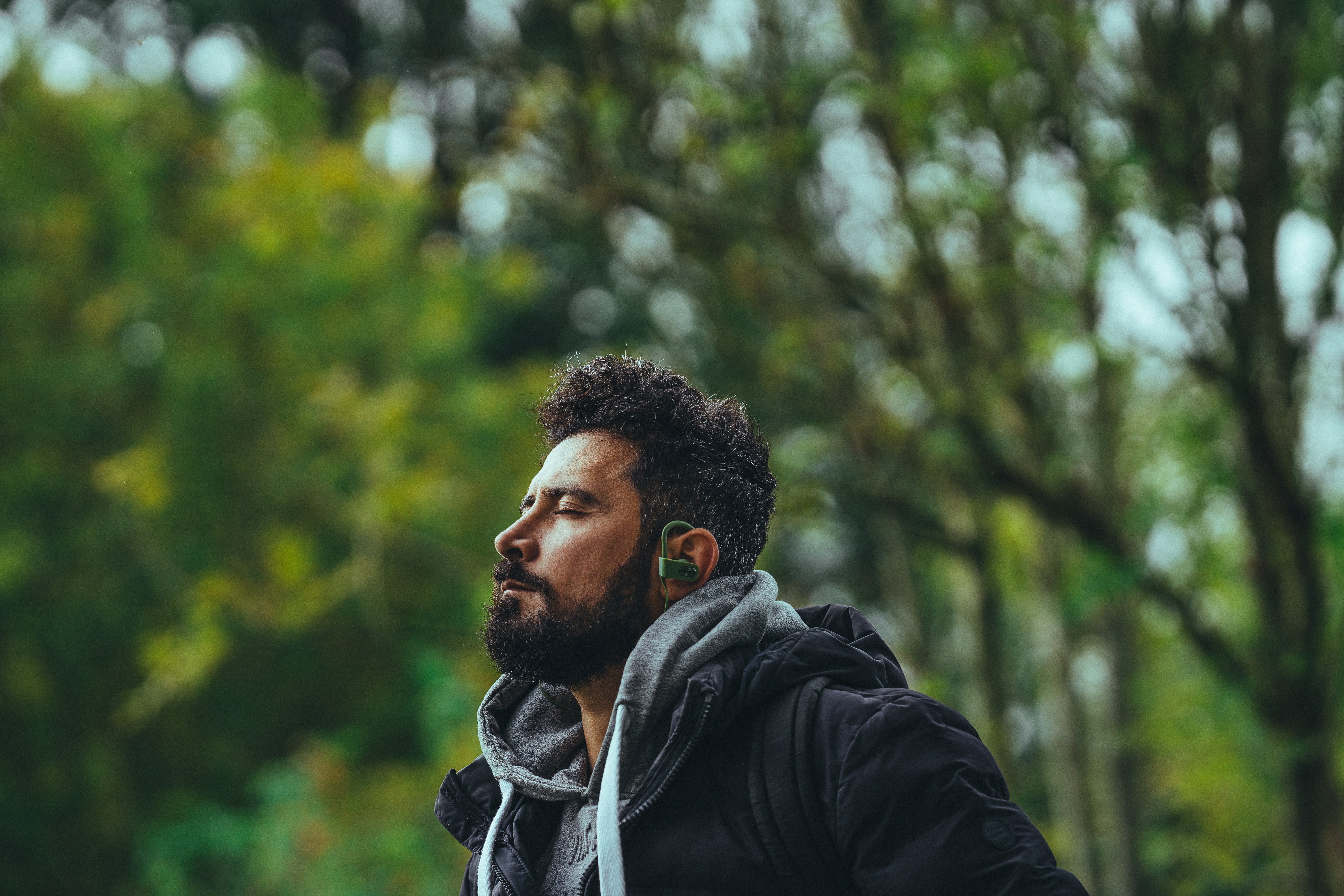 Thoughtful man listening to music in earbuds in park